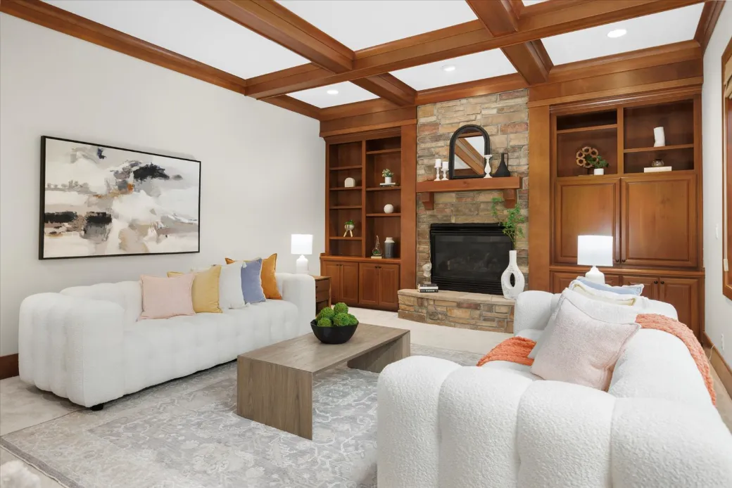 A modern living room in Seattle features two white sofas, a wooden coffee table, and a stone fireplace. Wooden shelves and abstract artwork adorn the space, impeccably designed by expert home stagers to create an inviting ambiance.